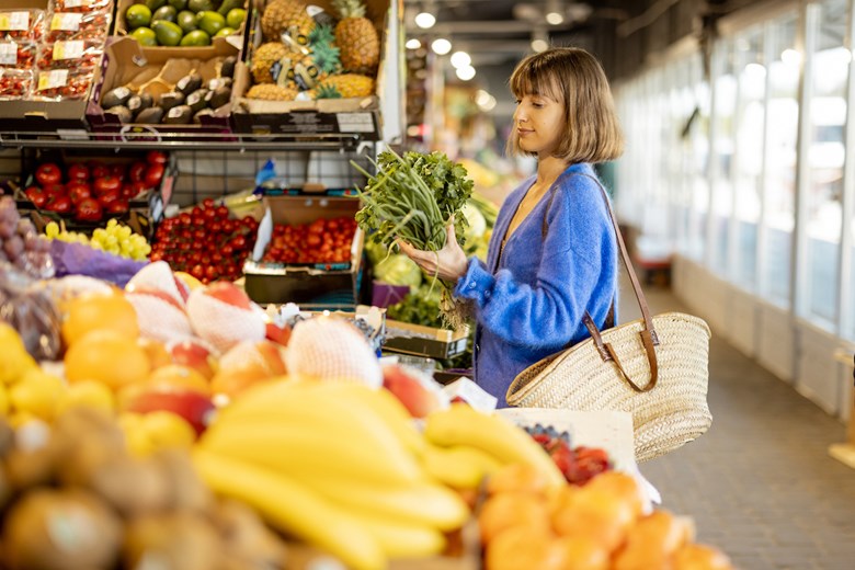 Mulher fazer compras num supermercado na secção das frutas e legumos com um cesto ecológico.