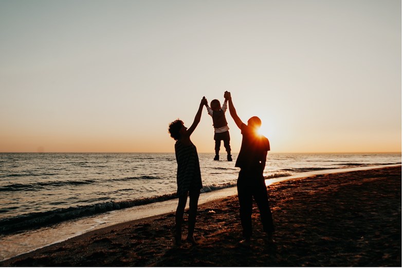 Família na praia ao pôr do sol. Pais levantam a criança pelos braços