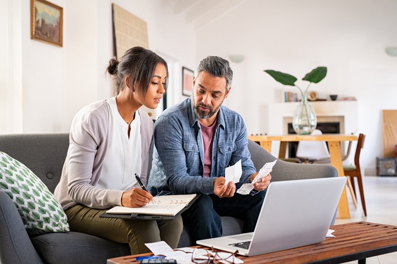 Um casal sentado no sofá a olhar para um computador portátil enquanto fazem contas às suas finanças.