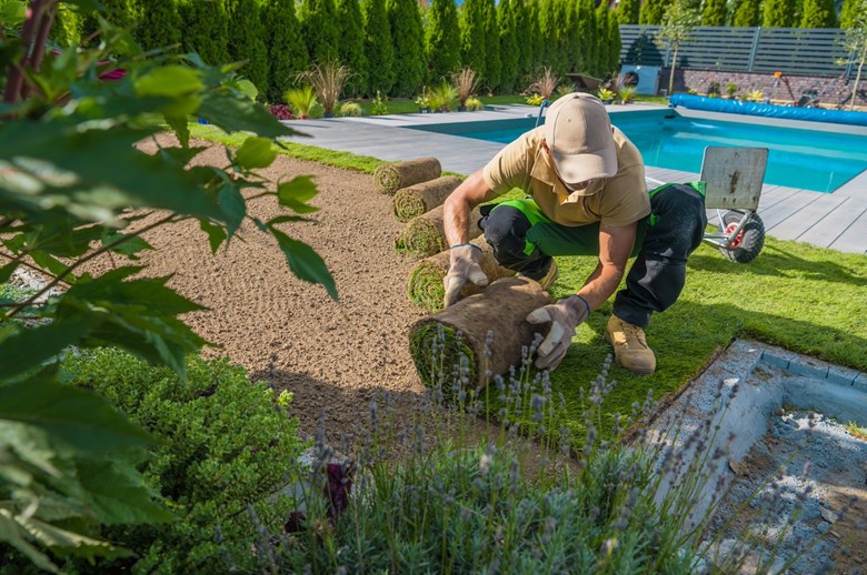 Jardineiro a estender a relva no exterior de uma casa ao pé da piscina.