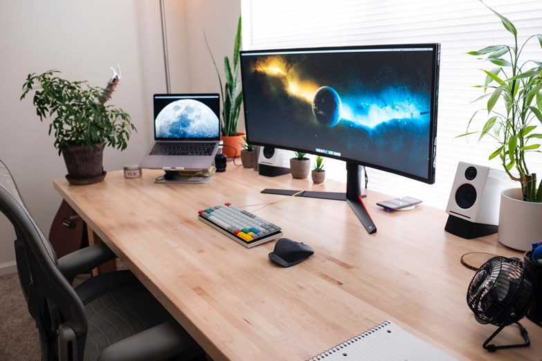 Estação de trabalho com um computador portátil e um ecrã, decorada em tom minimalista e com plantas, num escritório em casa.
