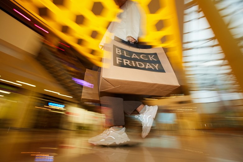 Pessoa em passo apressado num centro comercial, a carregar sacos de compras alusivos à Black Friday
