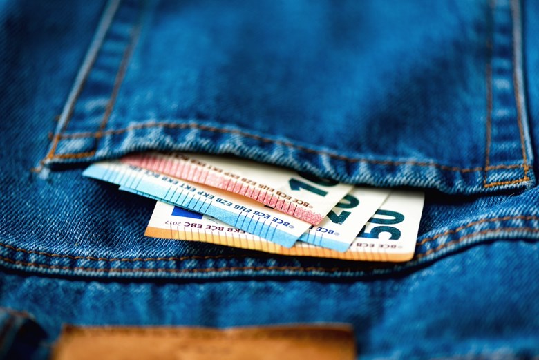 Notas de euro a sair de um bolso de umas calças de ganga.