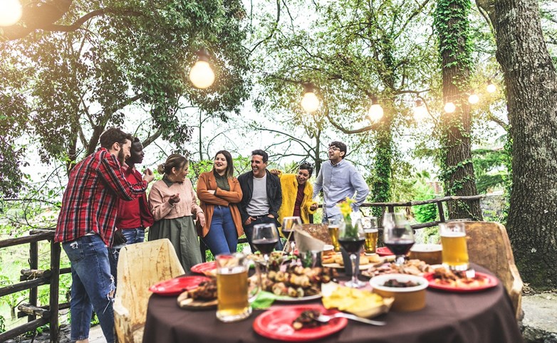Exterior. Grupo de amigos à conversa antes de se sentarem à mesa para irem comer um barbecue