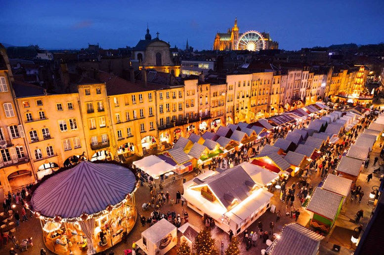 Mercado de Natal em Metz, em França, com bancadas iluminadas e a roda-gigante ao pé da Catedral ao fundo