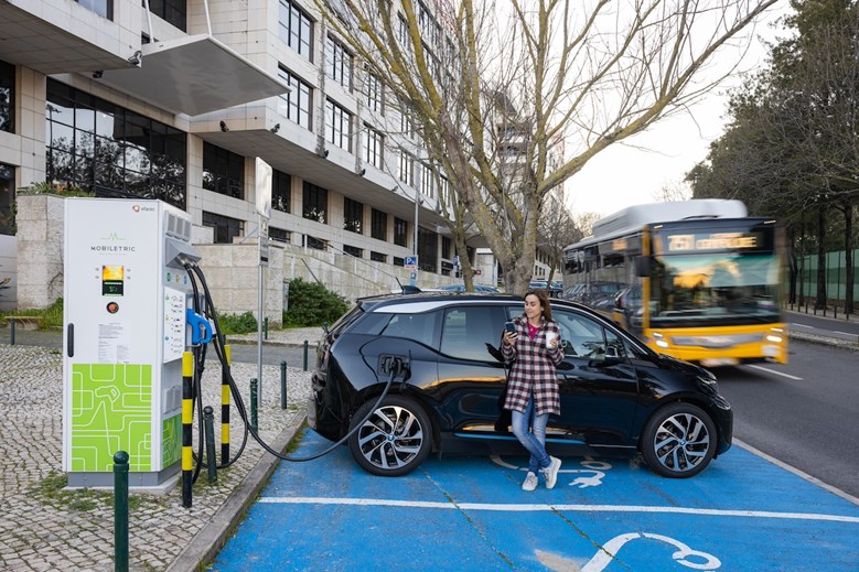Mulher encostada a um carro numa estação de carregamento de carros elétricos em Lisboa, Portugal.