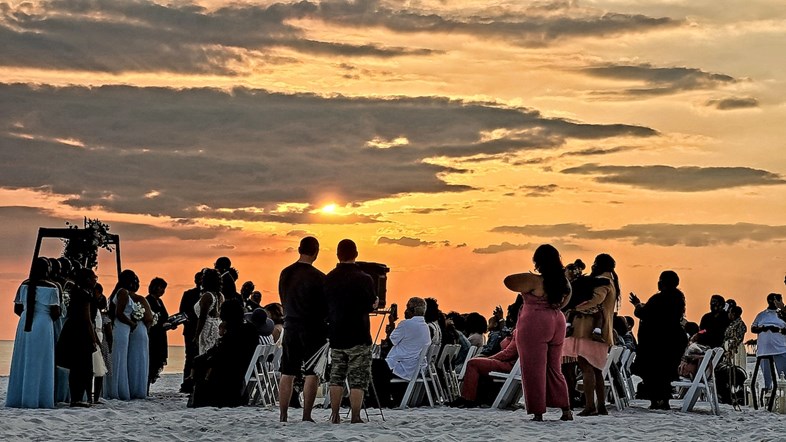 Celebração de um casamento na praia durante o pôr do sol, com o céu pintado de forma natural com um bonito alaranjado.