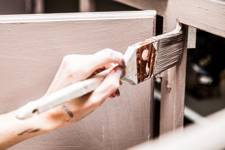Uma pessoa pinta cuidadosamente a porta de um armário com um pincel, dando uma nova vida a uma peça antiga.