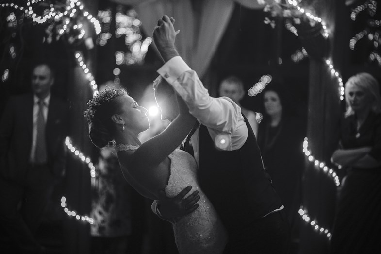 Noivos dançam no seu casamento sob o olhar atento dos convidados, imagem num estilo clássico a preto e branco.