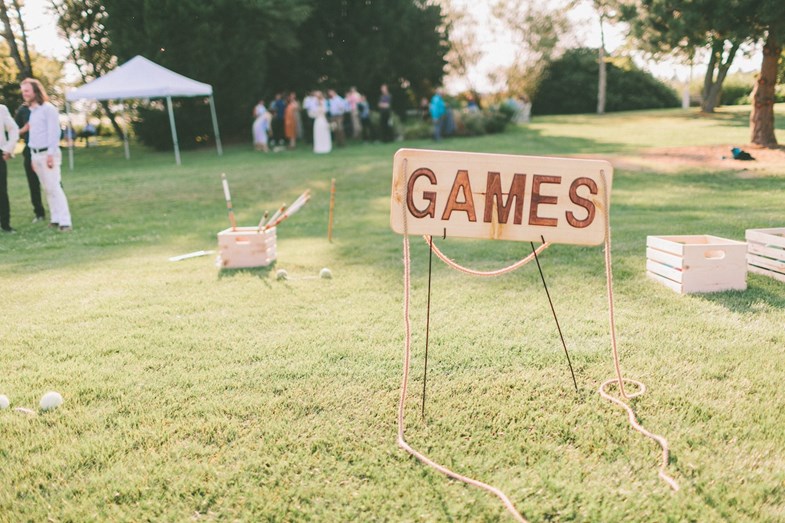 Exterior, recepção de um casamento. Tabuleta na relva a sinalizar aos convidados onde se podem divertir com jogos tradicionais.