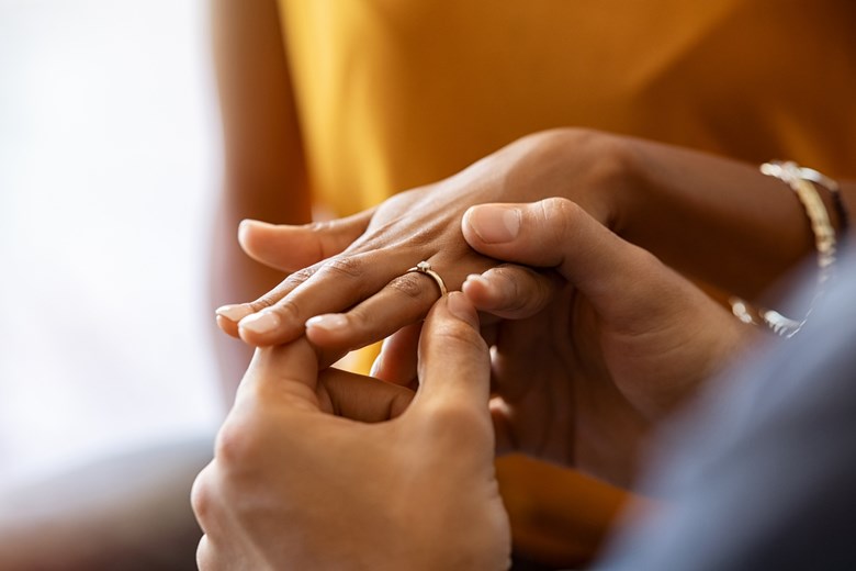 Homem segura a mão de uma mulher com o anel de noivado.