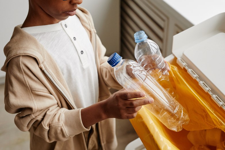 Criança faz reciclagem de plástico no ecoponto amarelo em casa.