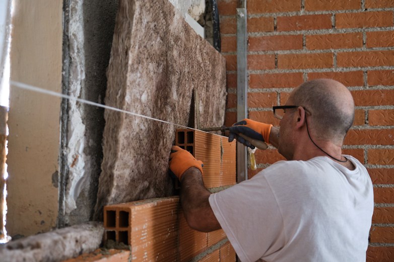 Homem aplica isolamento térmico nas paredes durante a construção de uma casa.