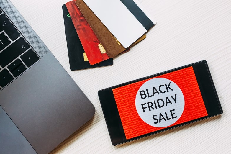 Telemóvel com a mensagem 'Black Friday Sale' e cartões de crédito ao lado de um computador portátil