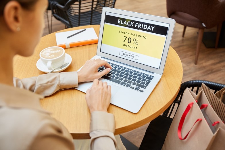 Mulher a usar um computador portátil num café de um centro comercial, com uma promoção de Black Friday exibida no ecrã