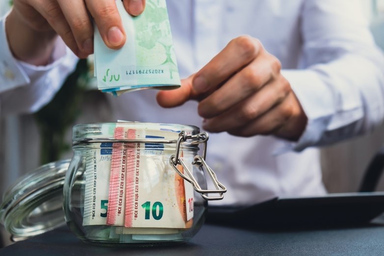 Homem coloca notas de euros numa jarra de vidro para aumentar as suas poupanças.