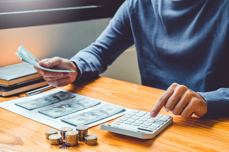 Homem a fazer contas com recurso à calculadora e com dinheiro na mão.