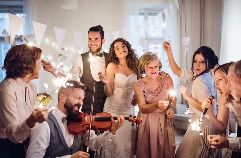 Grupo diverte-se numa festa de casamento. Um dos convidados toca violino e outra convidada canta ao microfone.
