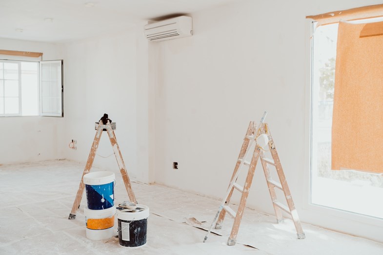 Sala com material de pintura e escadas.